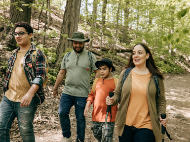 Family walking together on a forest trail surrounded by trees and natural greenery.